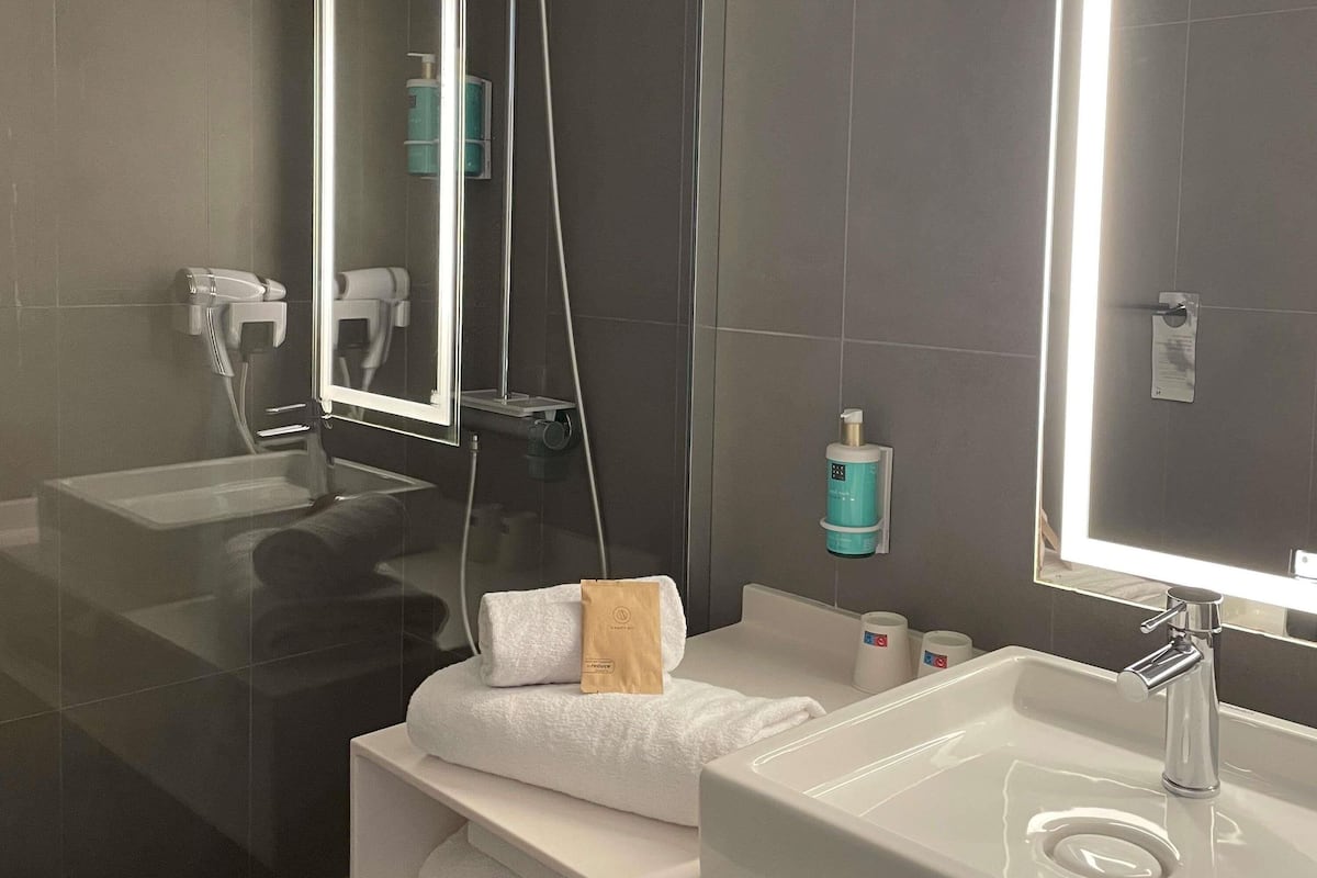 A modern bathroom with a large mirror, a sink, a towel, and a handheld showerhead.