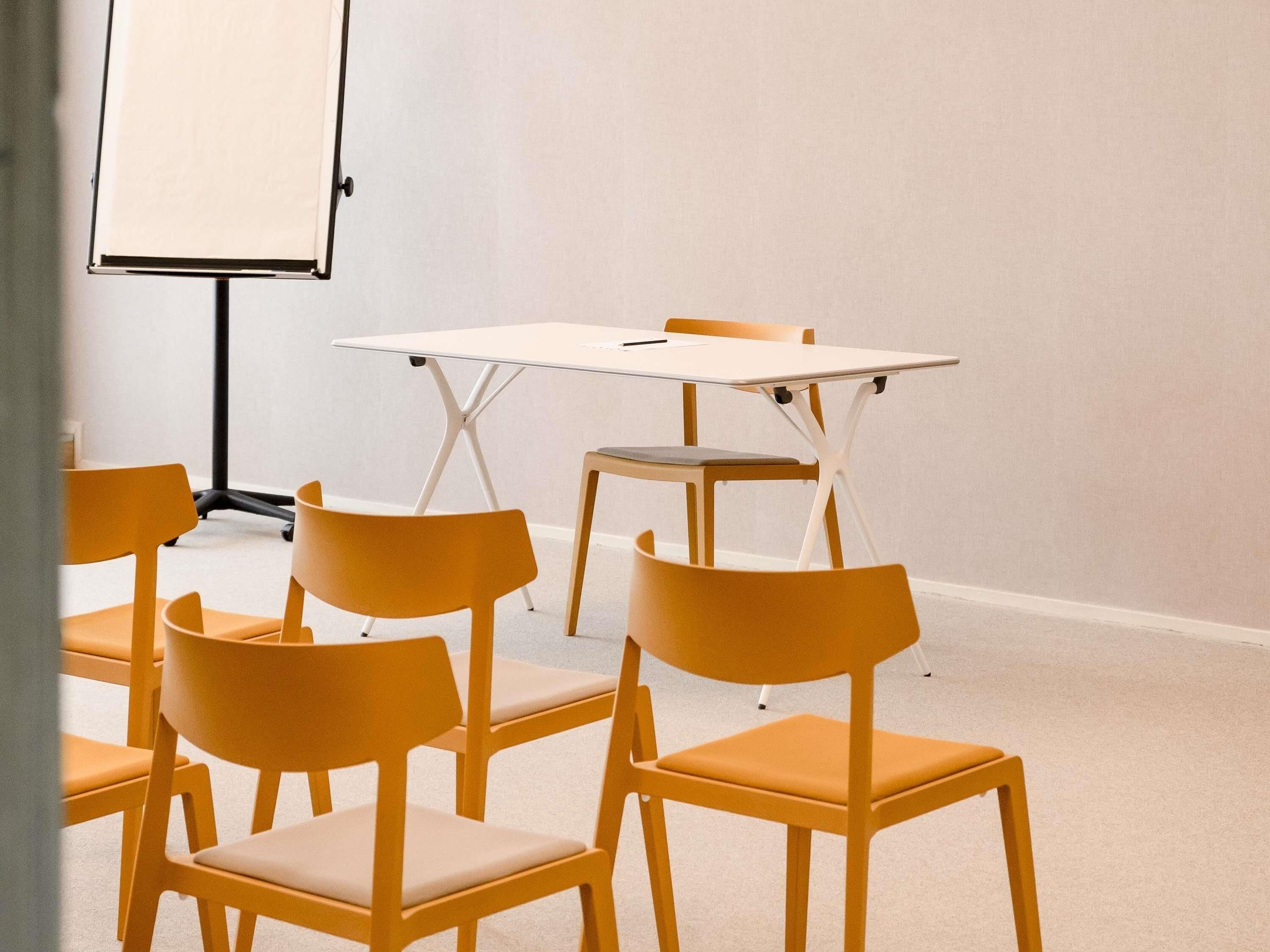 A conference room with a white table, four yellow chairs, and a whiteboard.