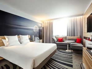 Una habitación de hotel moderna con una cama grande, un sofá, una mesita y un televisor.