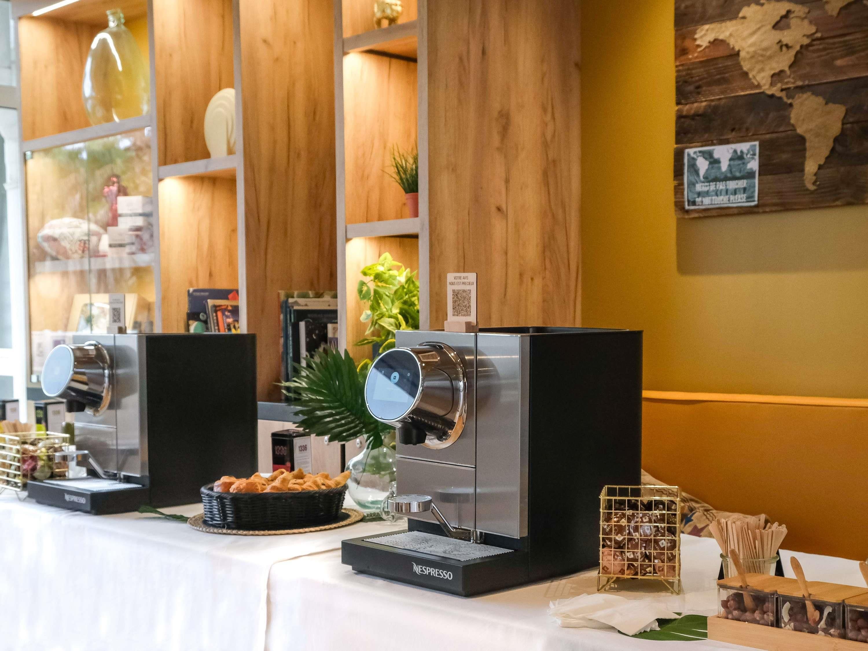 Una estación de café con dos máquinas Nespresso, una cesta de pasteles y una pequeña planta.