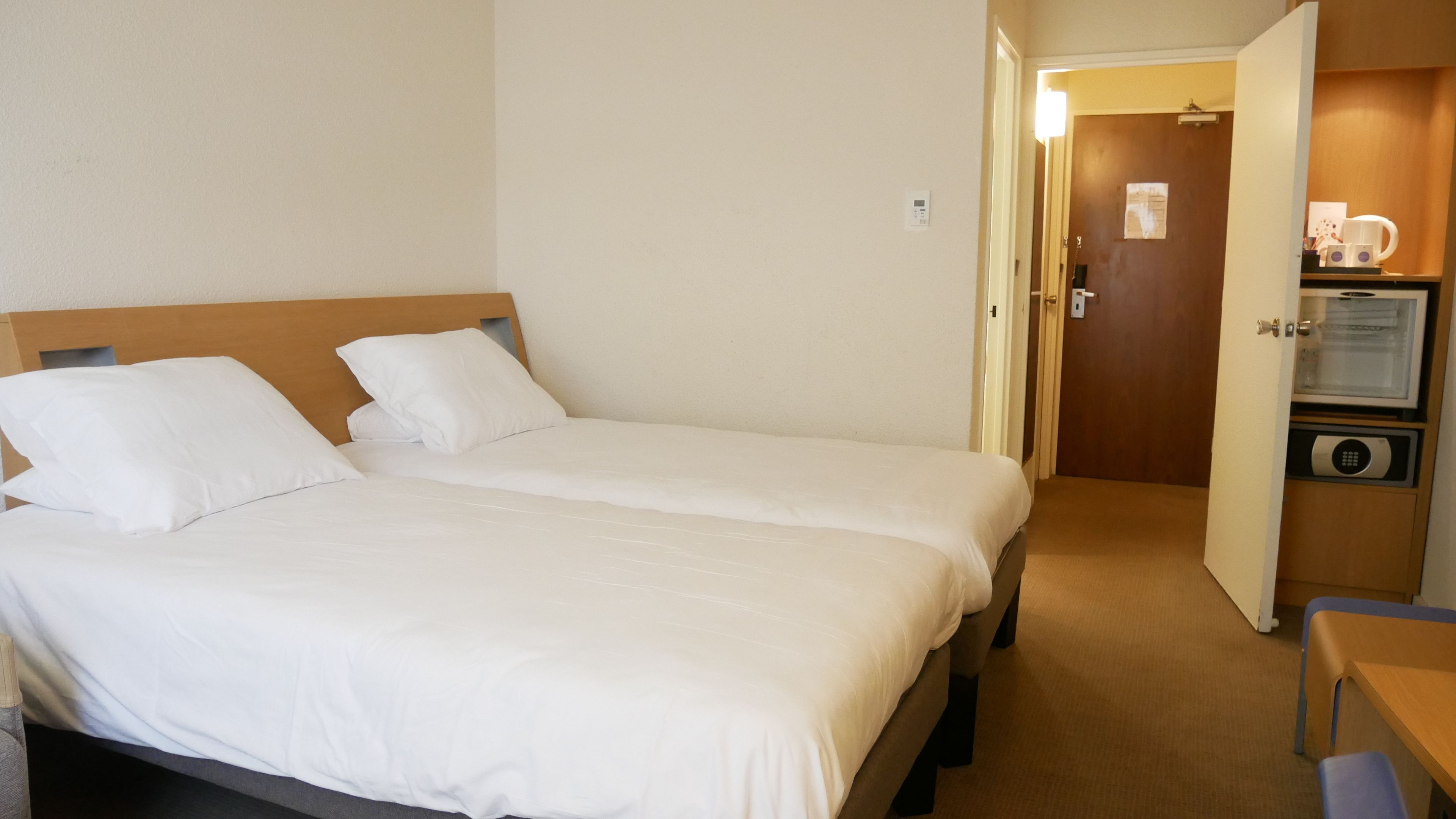 Habitació d'hotel amb dos llits, una taula de treball i un minibar.