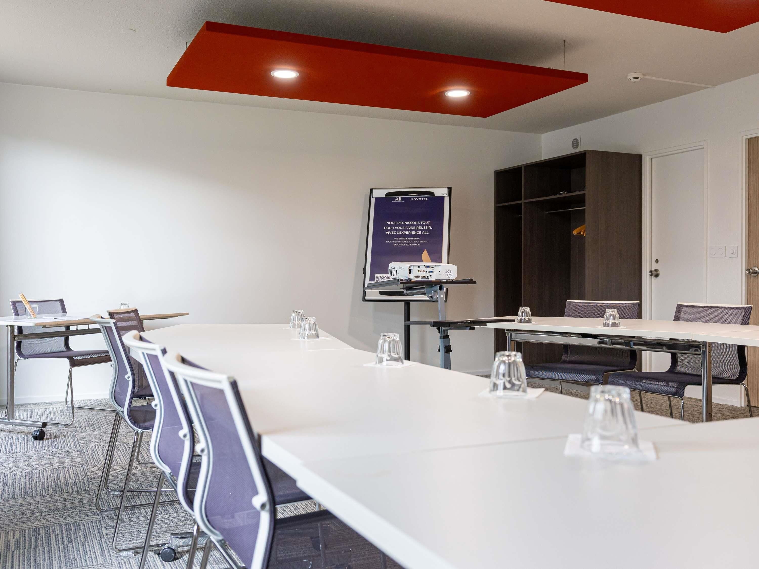 Un salón de conferencias con mesas y sillas blancas, y una pantalla para proyector.