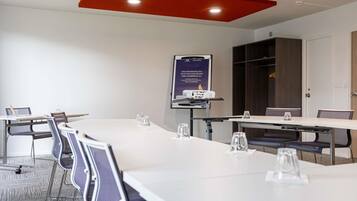 Un salón de conferencias con mesas y sillas blancas, y una pantalla para proyector.