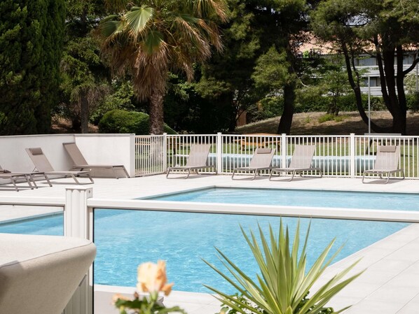 A rectangular swimming pool with a white deck, surrounded by a white fence. There are several lounge chairs along the pool's edge.