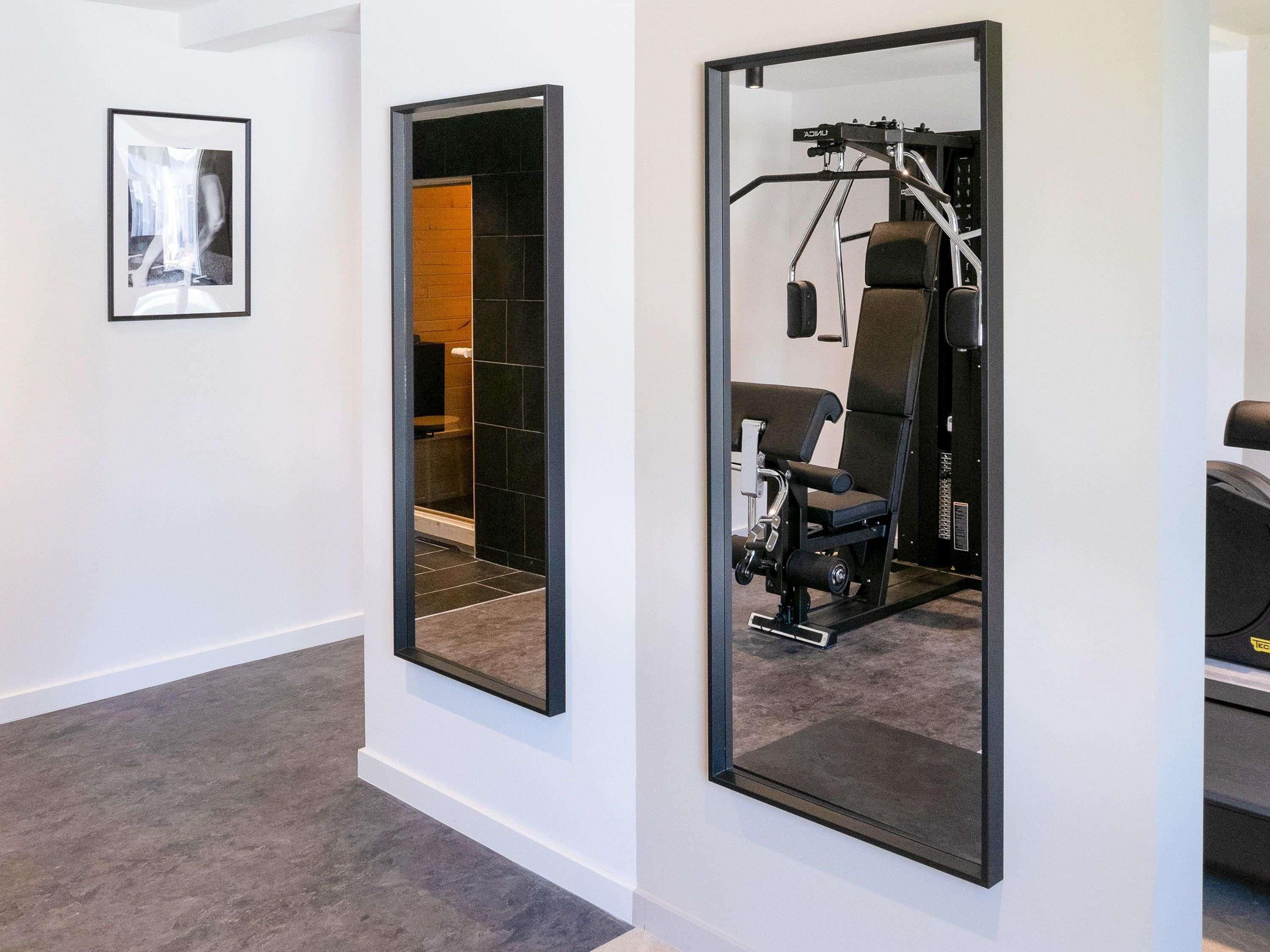 Un intérieur moderne comprenant un espace dédié à la salle de sport, avec des appareils d’exercice et un mur miroir qui agrandit visuellement l’espace.