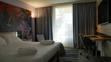 A hotel room with a large bed, a desk, a chair, a TV, and a window with curtains.