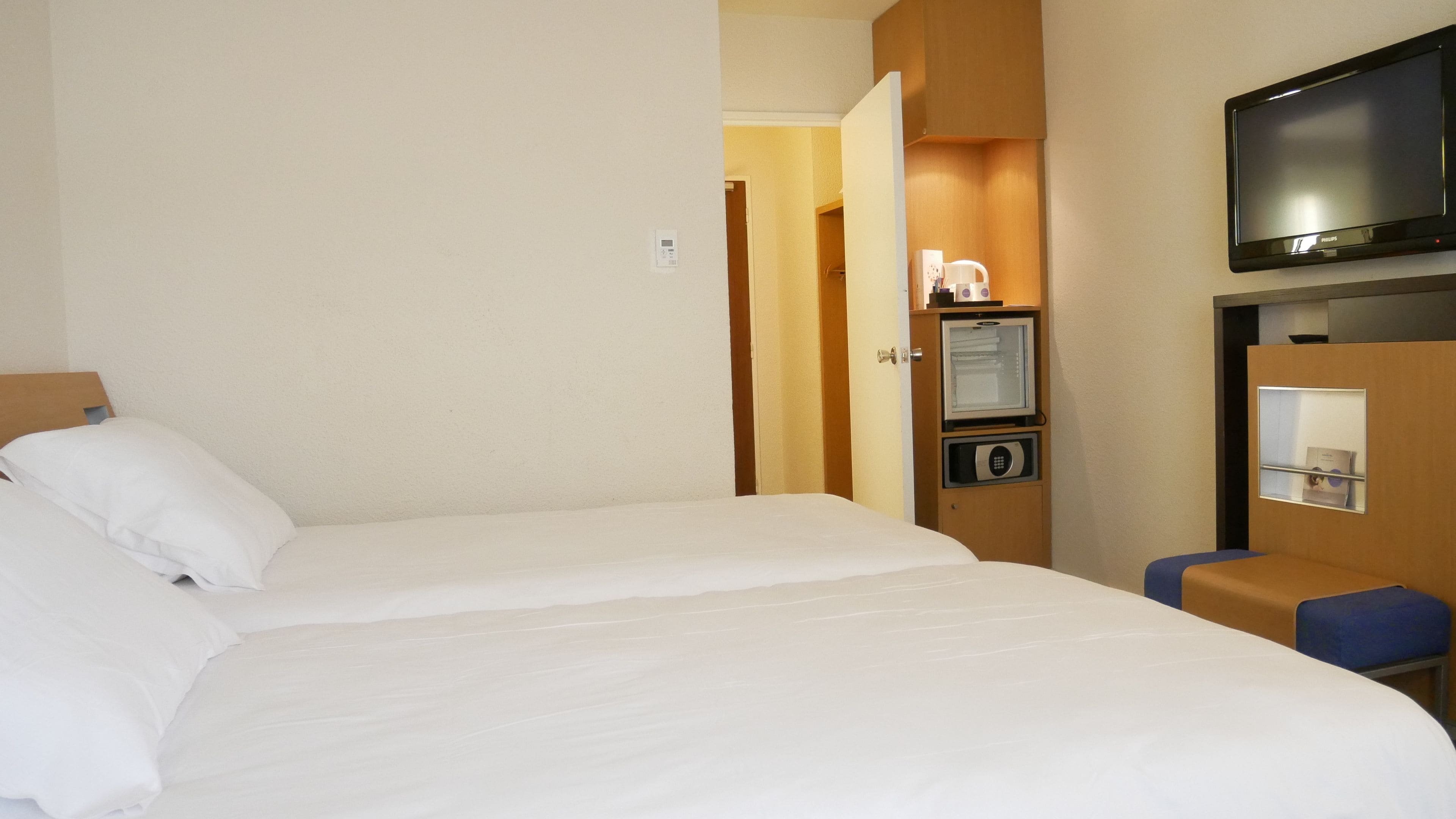 Una habitación de hotel con cama, televisión, minibar y un pequeño espacio de descanso.