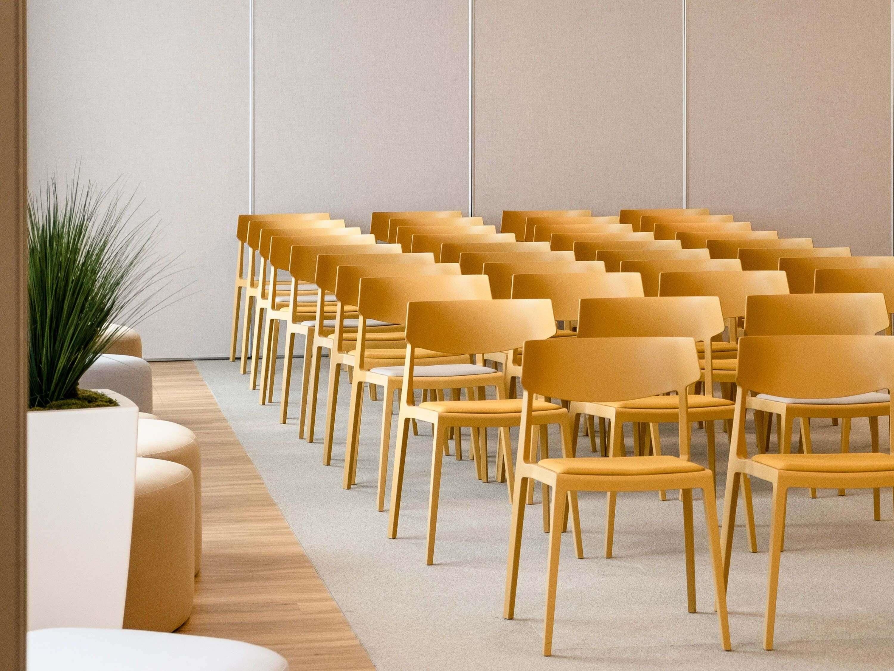 A row of yellow chairs arranged in a semi-circle facing a white wall.