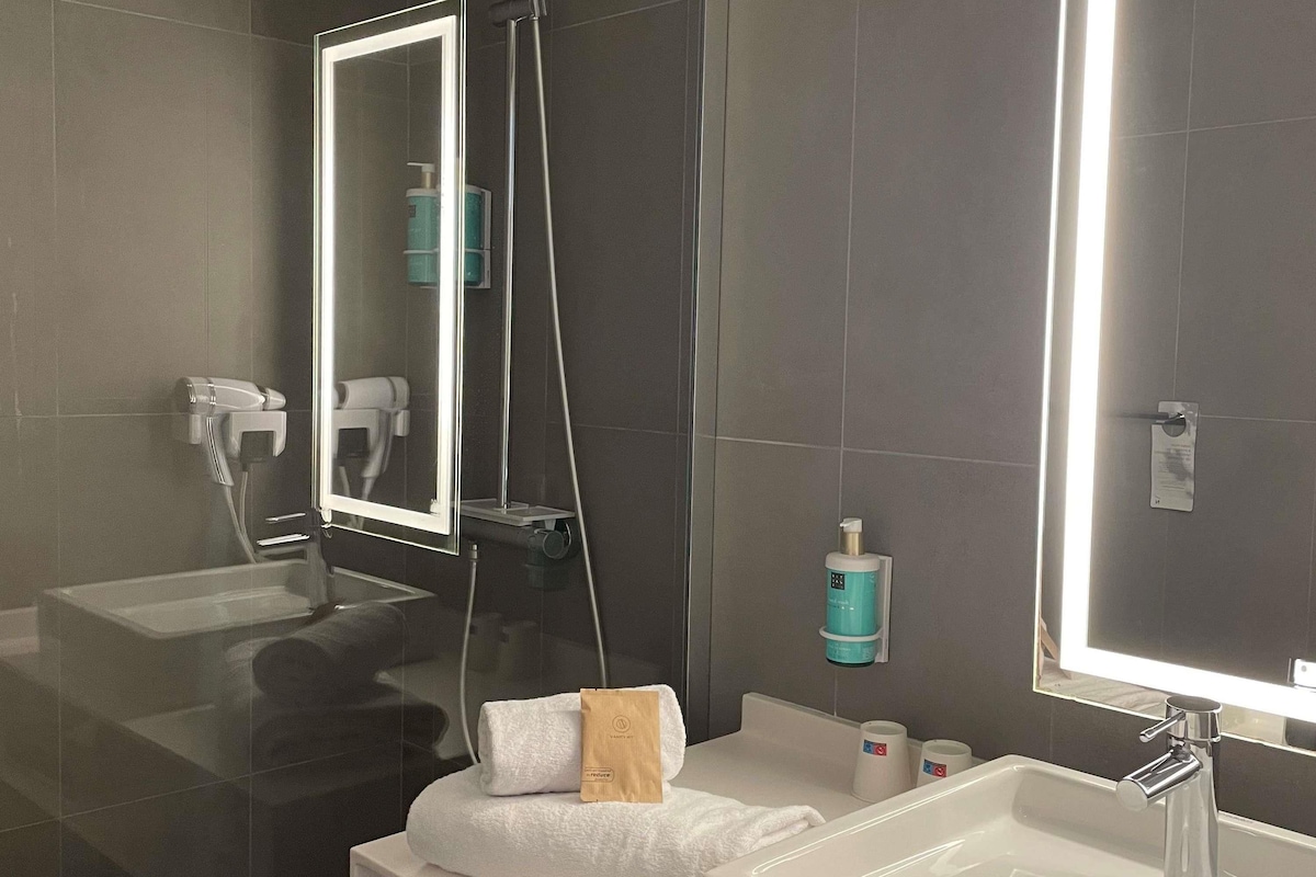 A modern bathroom with a large mirror, a white sink, and a towel rack.