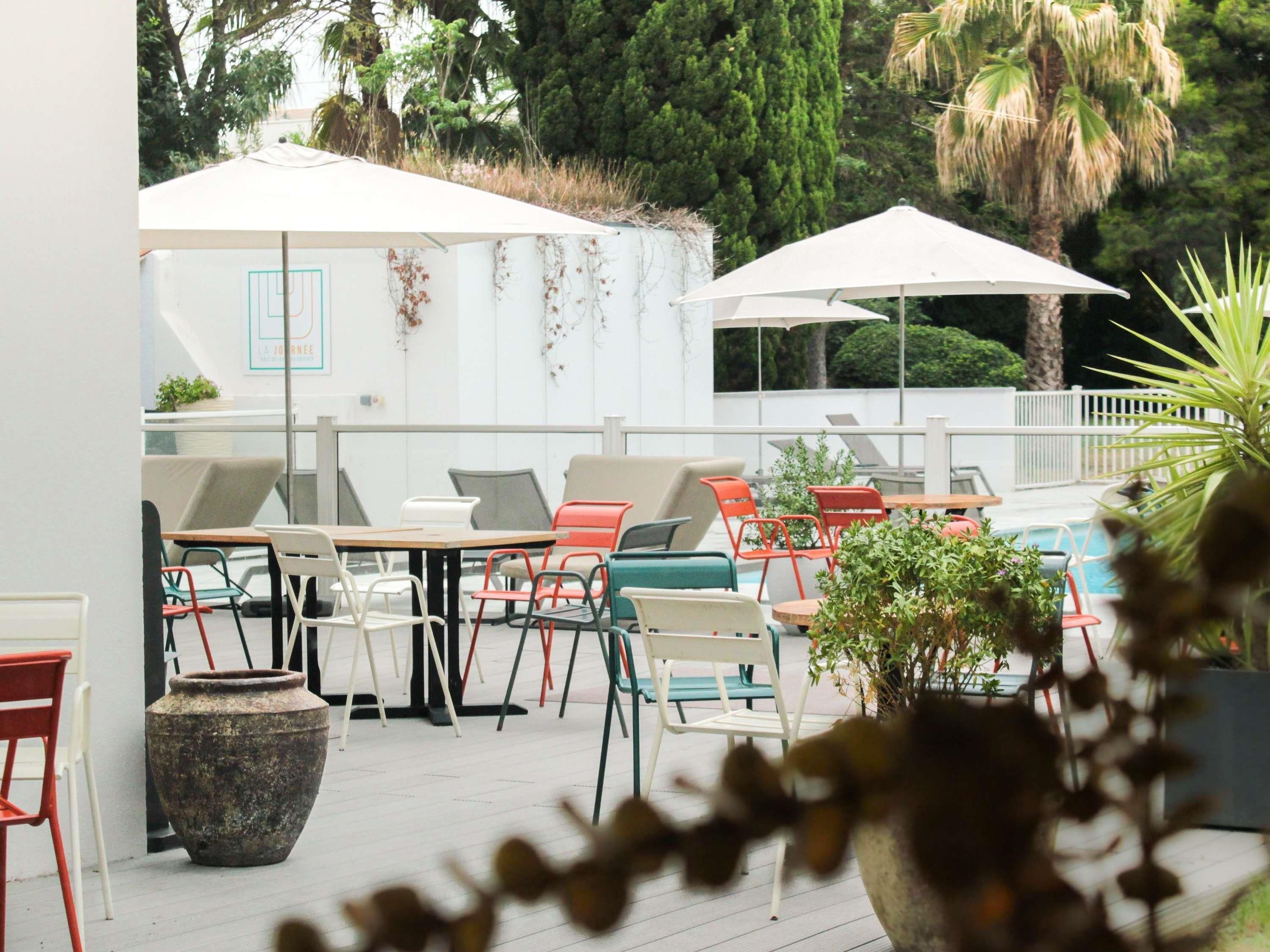 An outdoor seating area with tables and chairs, umbrellas, and a pool in the background.