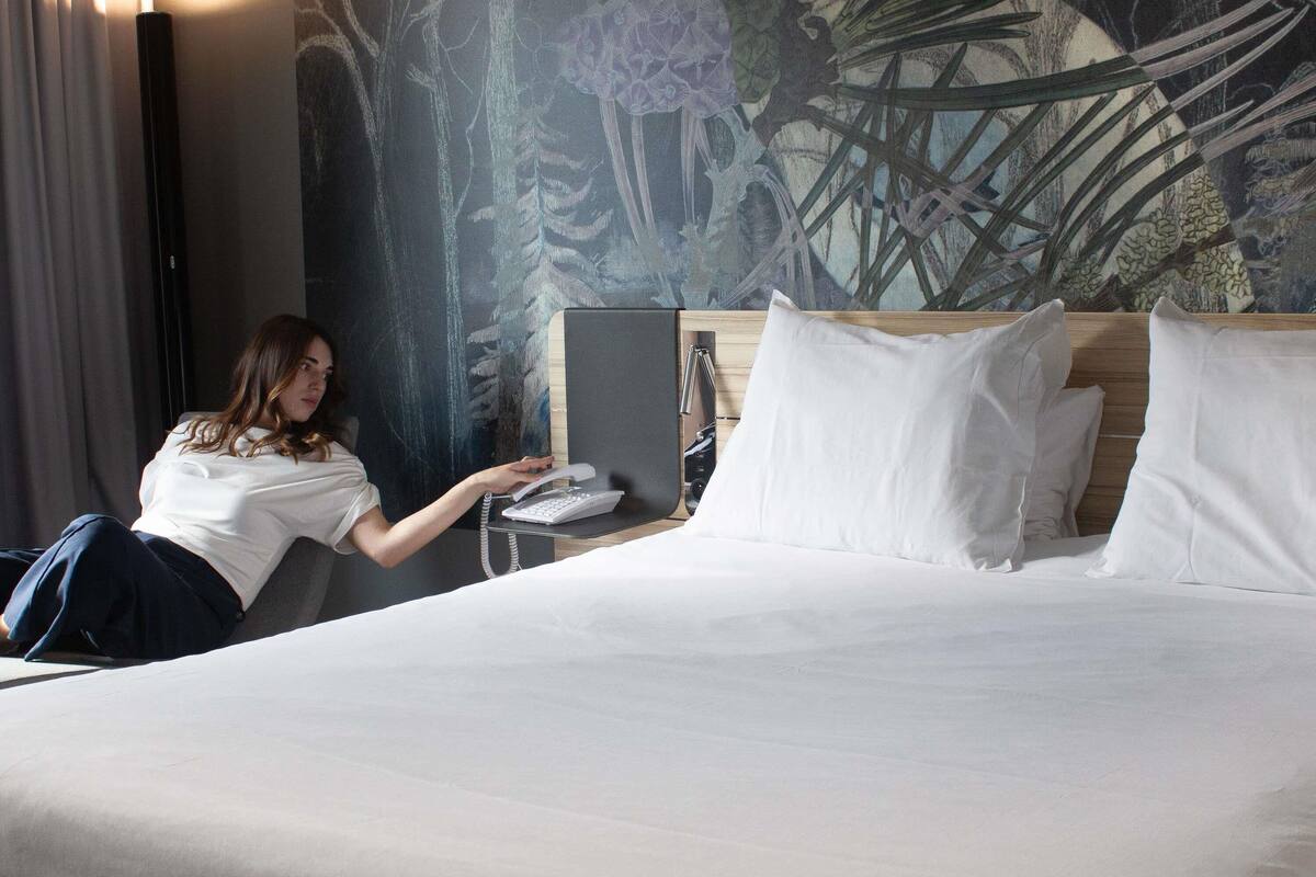 A hotel room with a bed, a desk with a phone, and a large wall mural.