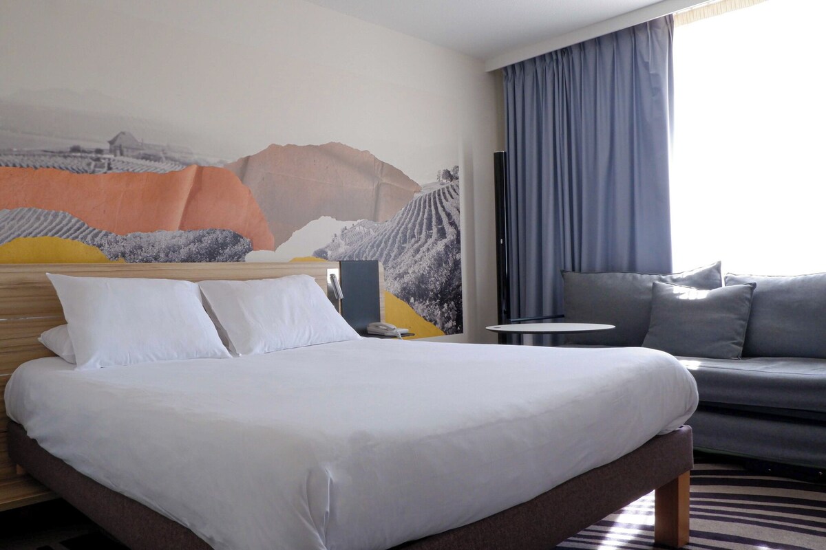 Una habitación de hotel con una cama grande, un sofá, una mesita redonda y un mural en la pared.