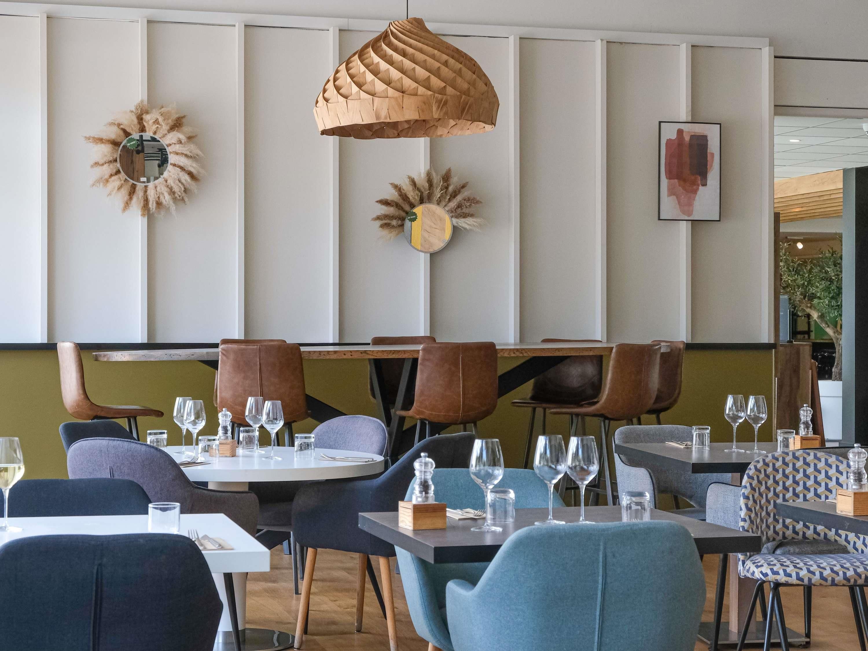 A restaurant interior with round tables, brown leather chairs, and a hanging wooden pendant light.