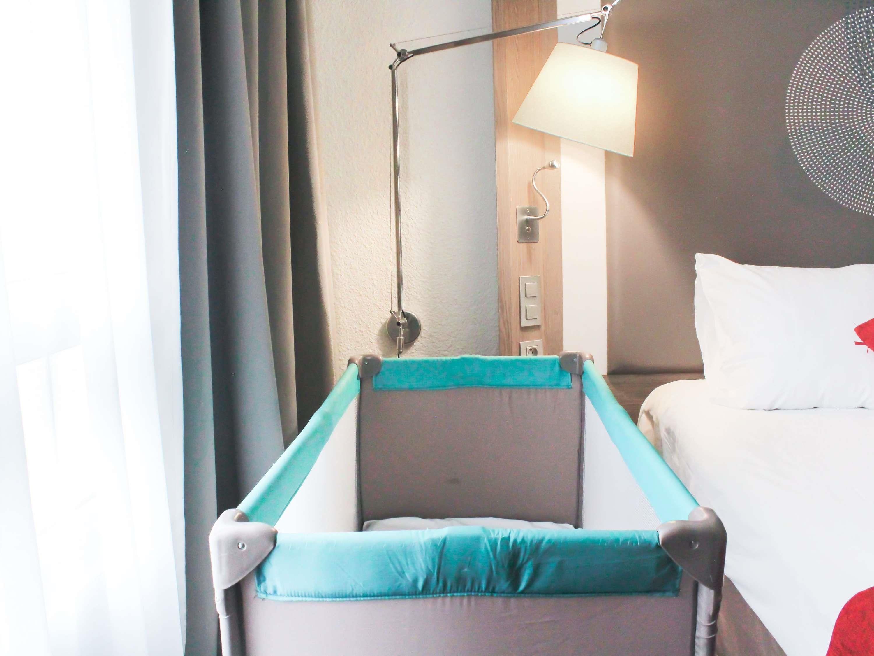 Una habitación de hotel con una cama, una mesita de noche, una lámpara y una cuna.