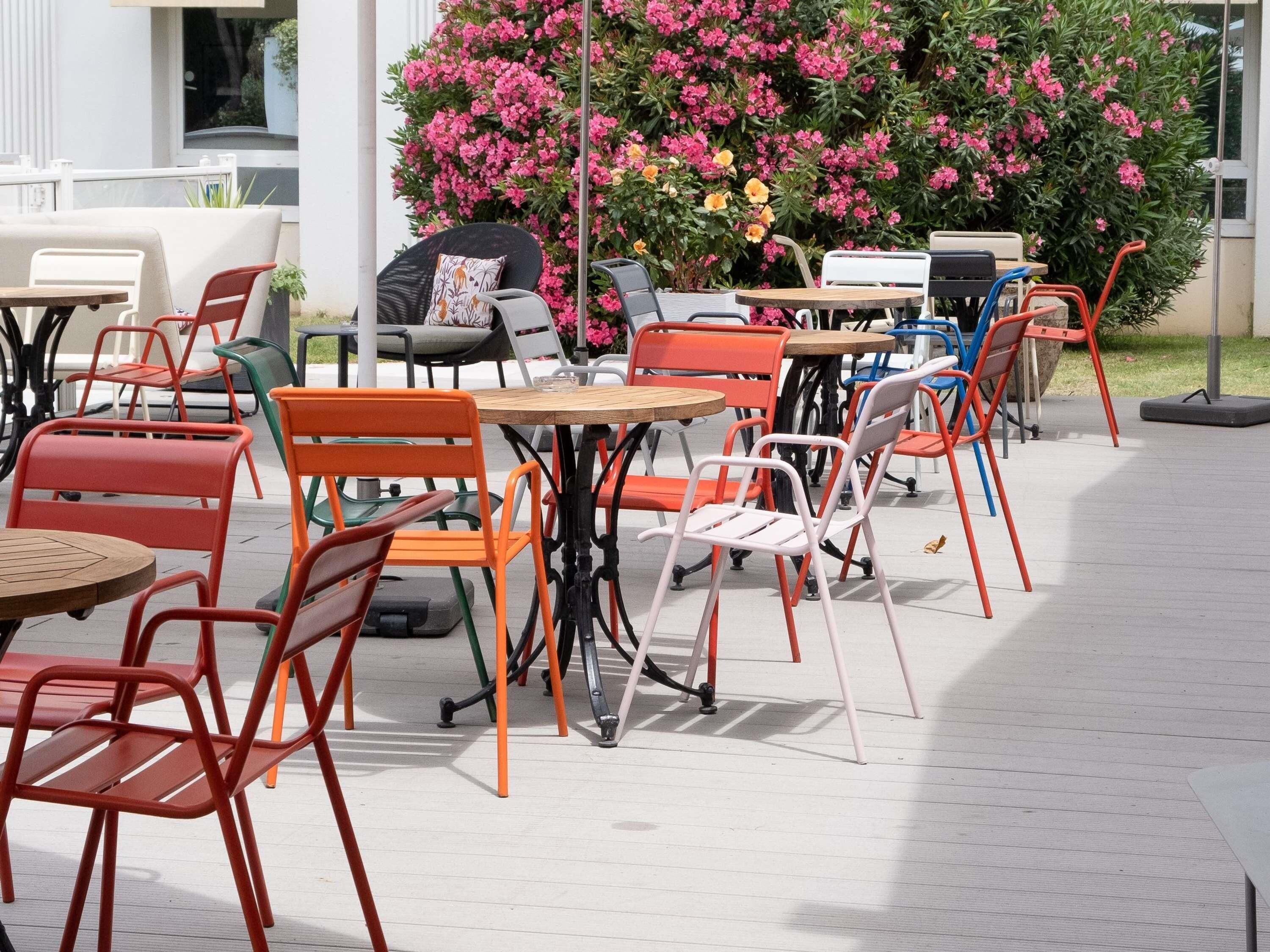 Un espace extérieur aménagé avec plusieurs tables et chaises, entouré d’une végétation luxuriante et de plantes en fleurs.