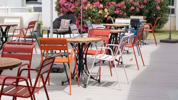 Un espace extérieur aménagé avec plusieurs tables et chaises, entouré d’une végétation luxuriante et de plantes en fleurs.