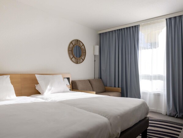 A hotel room with a large bed, a sofa, a mirror, and a view of the outdoors.