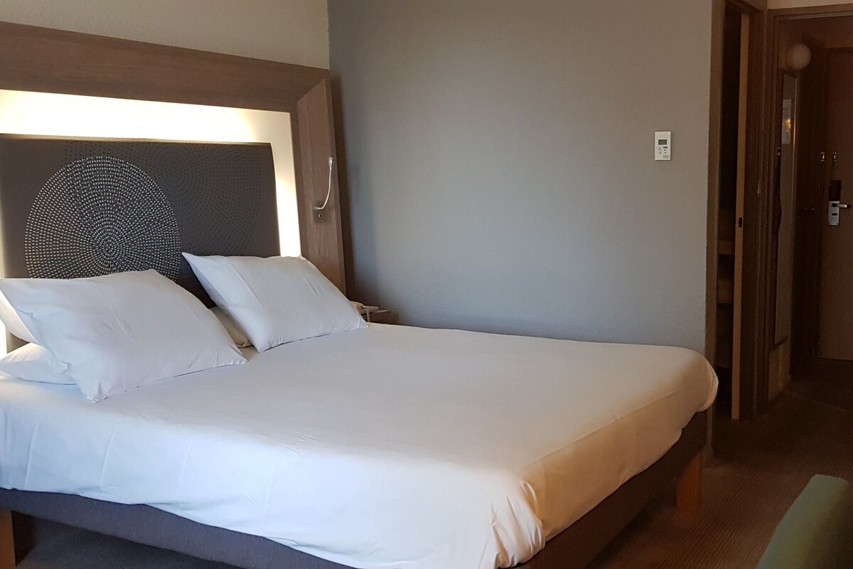 Una habitación de hotel con una cama, una mesita de noche, un escritorio pequeño y un refrigerador.