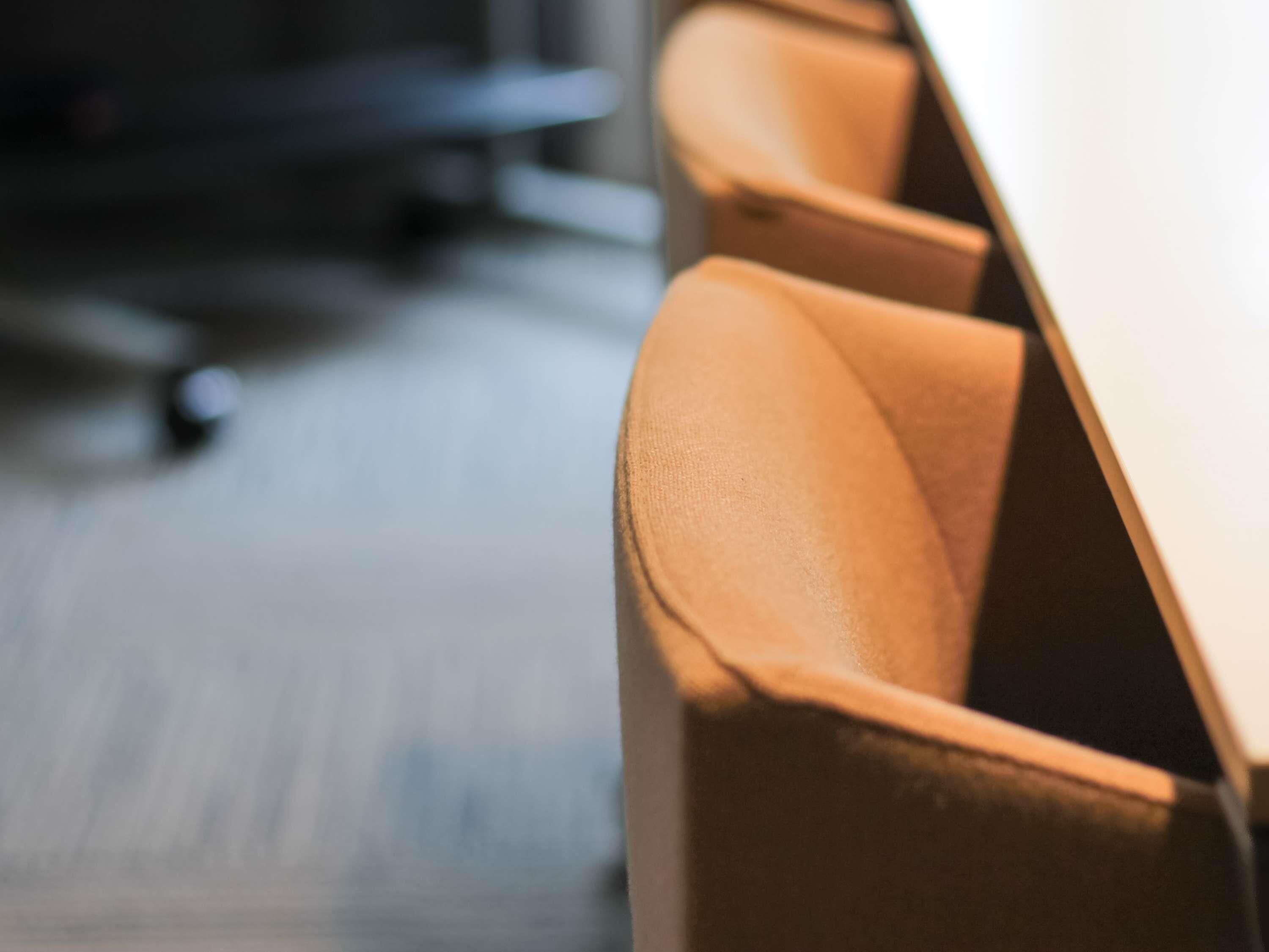 A close-up of a brown leather chair with a high backrest, positioned in a room with a wooden floor.