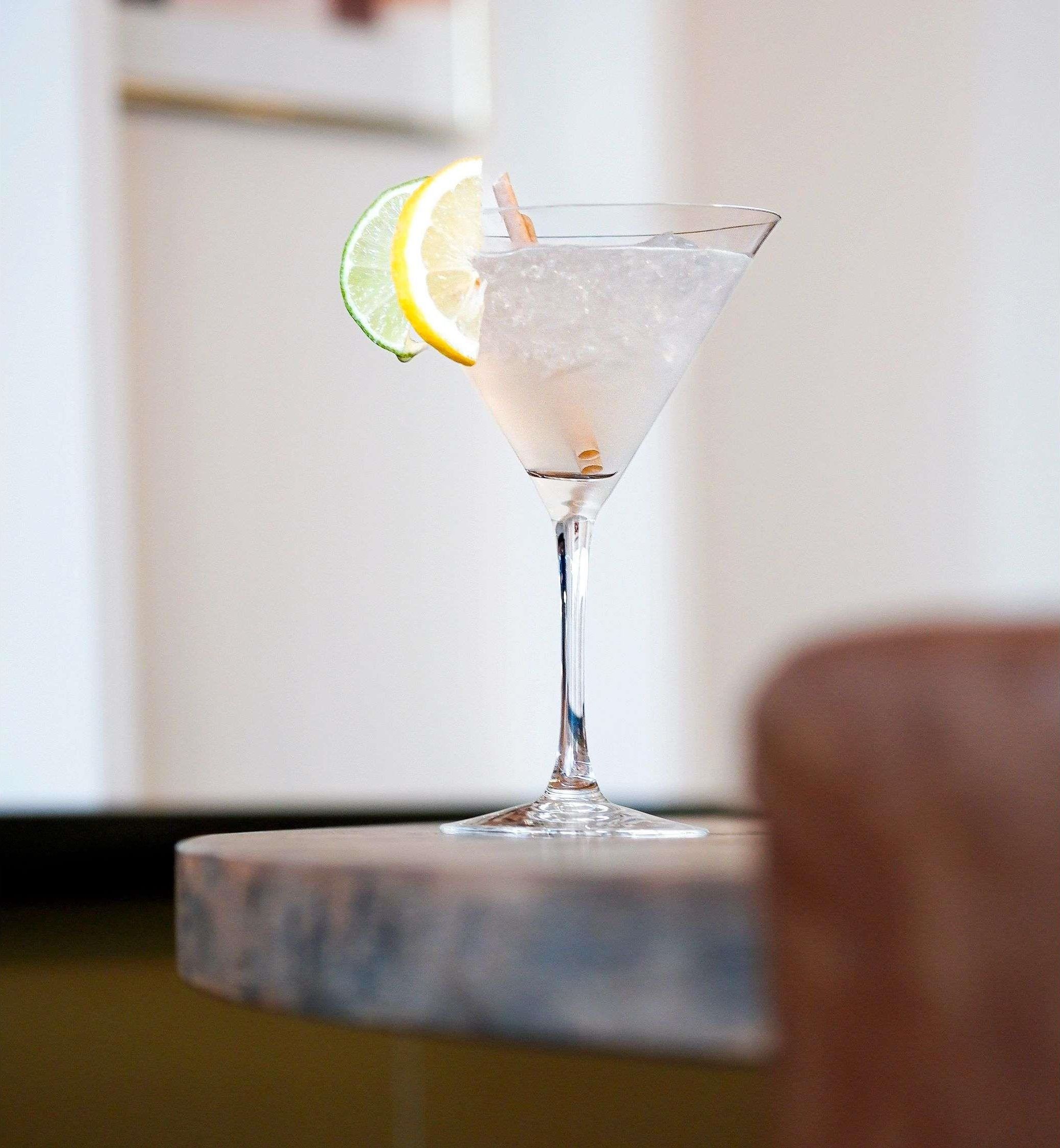 Ein Martini-Glas mit Eiswürfeln und Zitronenscheibe auf einem Marmortisch.