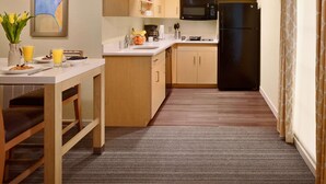 A compact kitchen with wooden cabinets, a black refrigerator, and a microwave. There is a dining table with breakfast items and a vase of flowers. - Sonesta ES Suites Somerset (Somerset)