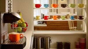 A kitchen with a coffee machine, a fruit bowl, and a shelf with colorful cups and saucers. - Sonesta ES Suites Somerset (Somerset)