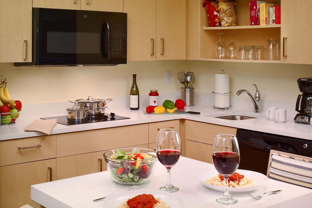 Una cocina moderna con microondas, estufa y lavamanos. Hay dos platos de pasta y dos copas de vino tinto sobre la encimera.