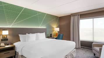 Ein Hotelzimmer mit einem großen Bett, einem Schreibtisch mit Lampe, einem Sessel und Blick auf die Stadt durch das Fenster.