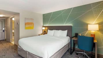 A hotel room with a large bed, a desk with a chair, a nightstand, and a wall-mounted lamp.