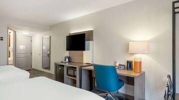 A hotel room with two beds, a desk with a computer, a TV, a lamp, and a microwave.