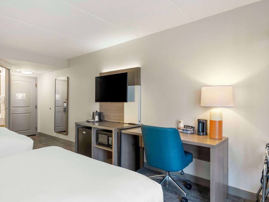 A hotel room with two beds, a desk with a computer, a TV, a lamp, and a microwave.