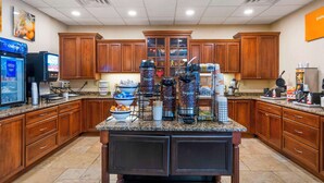 A hotel kitchen with wooden cabinets, granite countertops, and a coffee station with various coffee makers and containers. - Comfort Inn & Suites Watertown - 1000 Islands (Watertown)