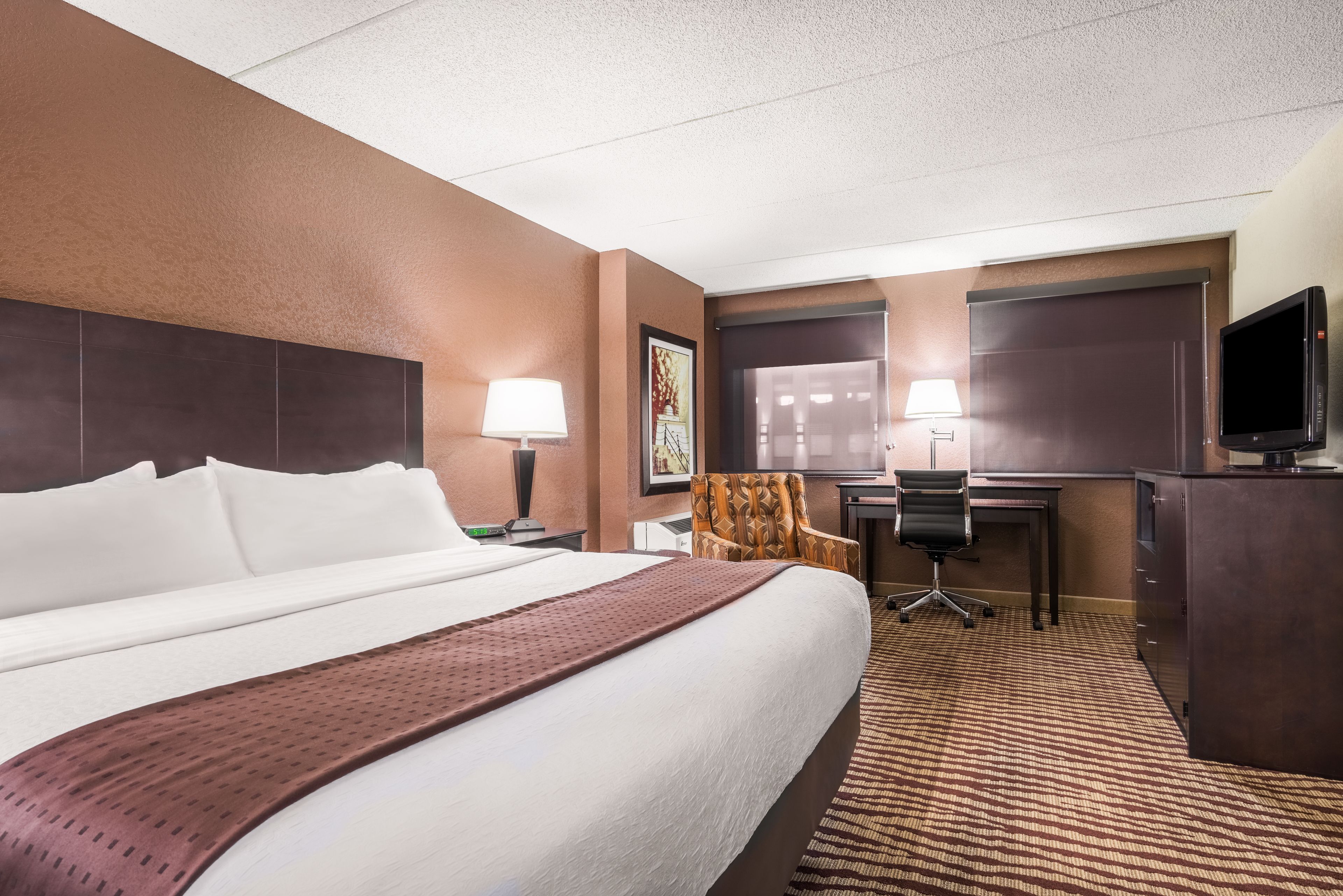 A hotel room with a large bed, a desk, a chair, a television, and a lamp.
