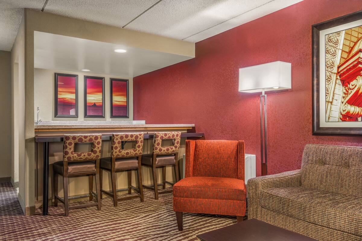 A hotel room with a bar area, a sofa, and a patterned carpet.