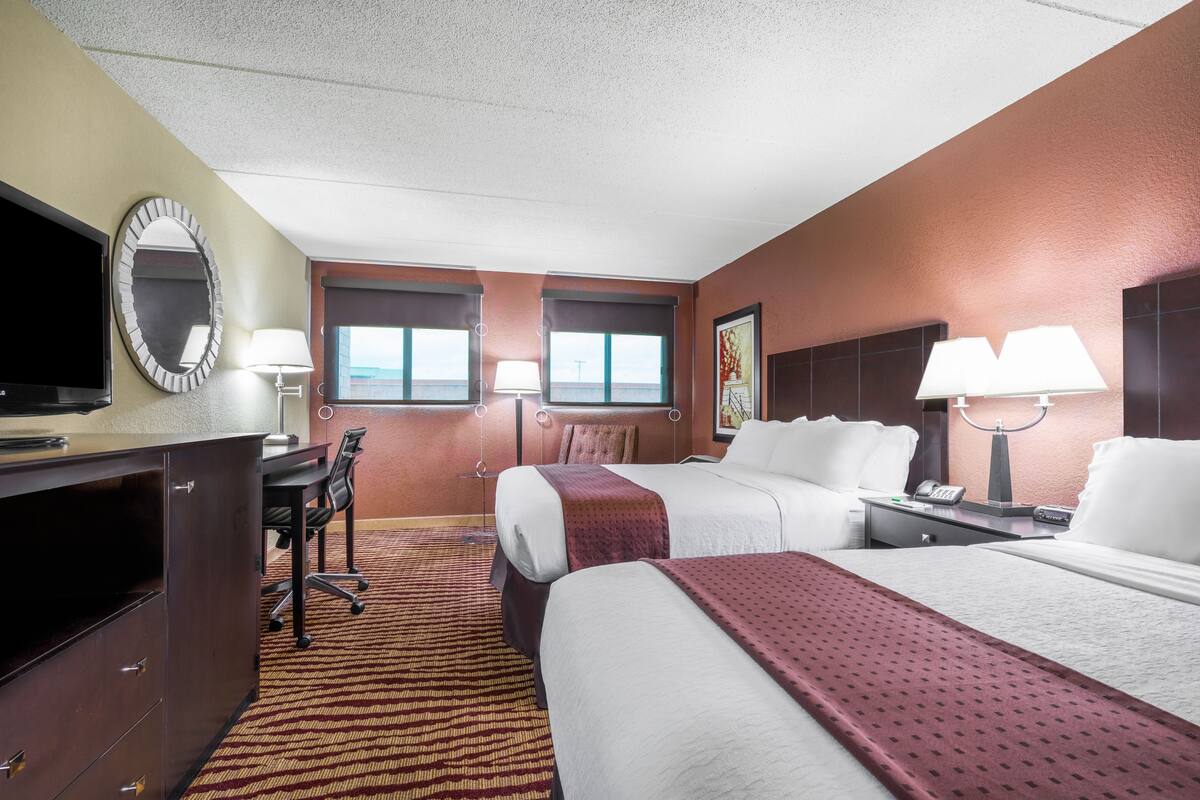 A hotel room with two beds, a desk, a TV, and a window with a view.