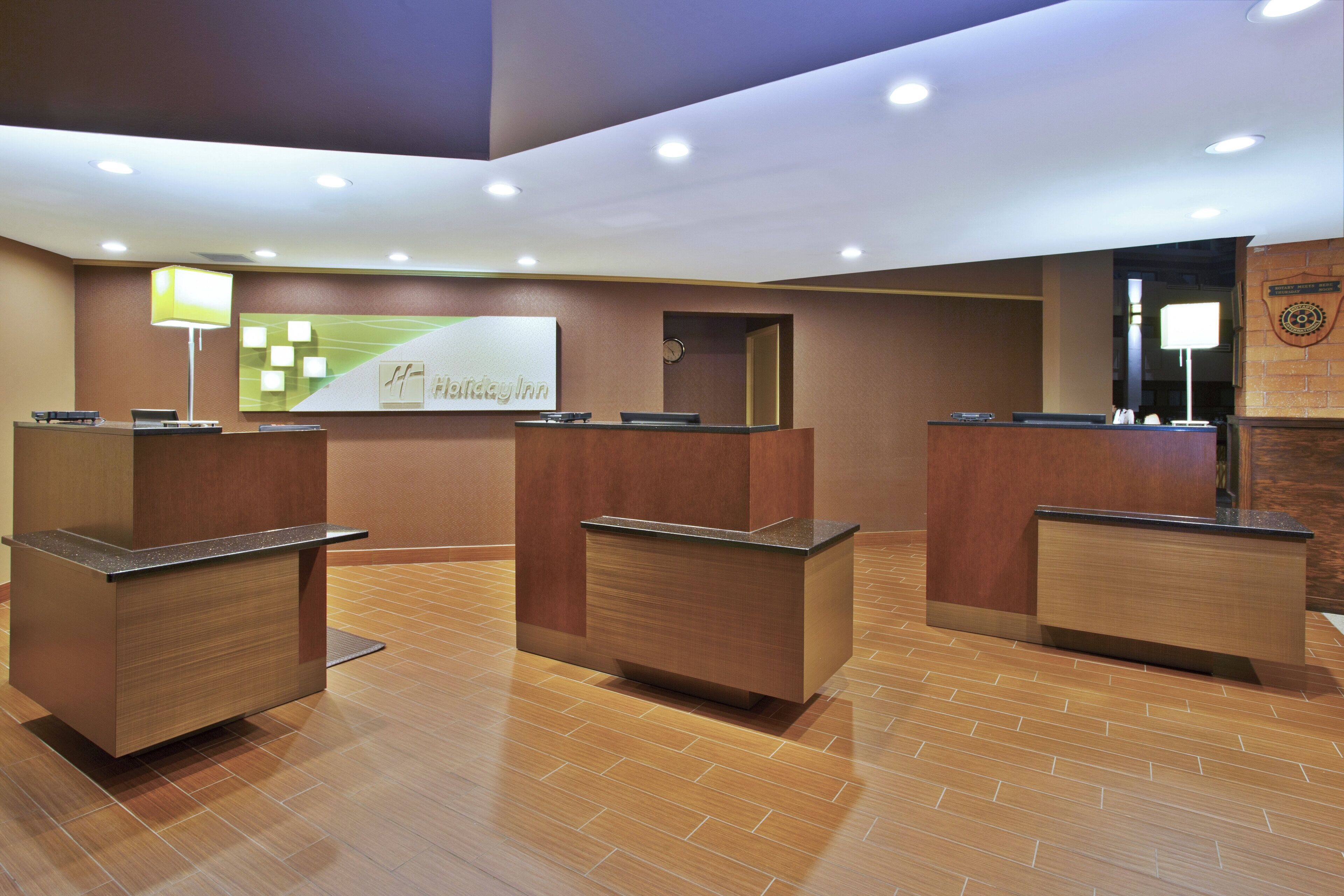 Una zona de recepció amb tres taulells de fusta, un rellotge i un rètol de Holiday Inn.