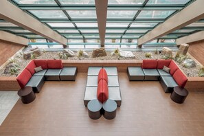 A modern outdoor seating area with a glass ceiling, featuring a sectional sofa and round tables.