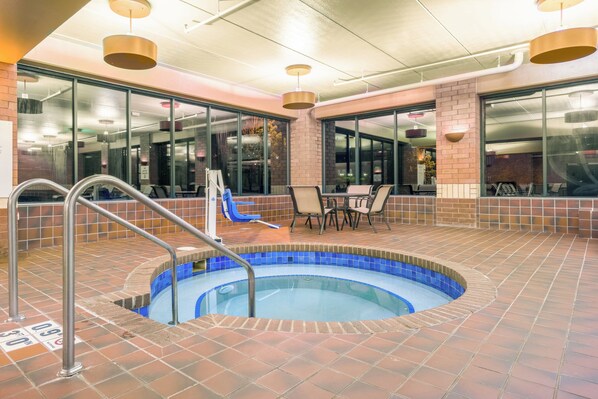 A pool area with a hot tub, lounge chairs, and a table.
