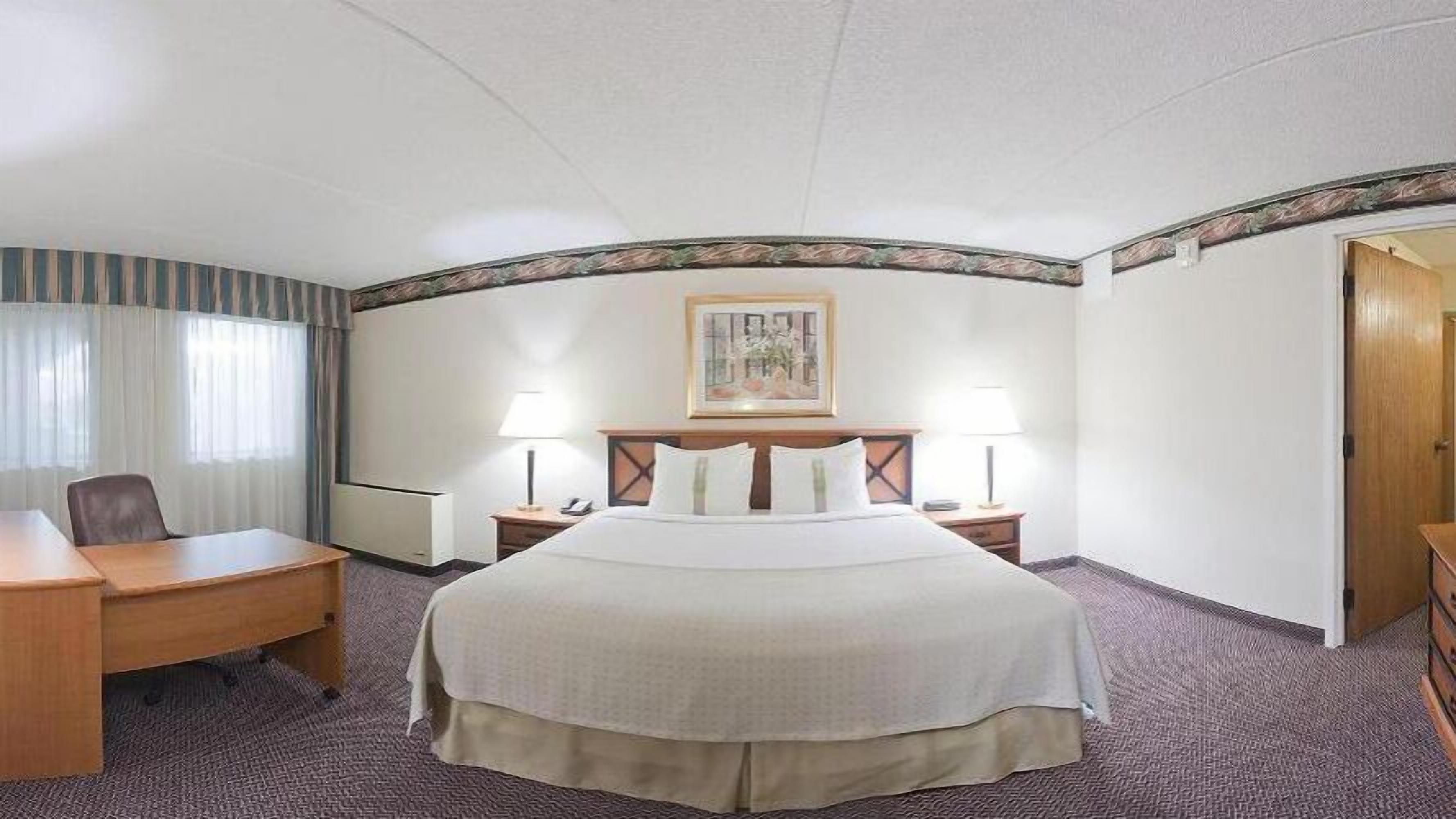 Ein Hotelzimmer mit einem großen Bett, zwei Nachttischen mit Lampen, einem Schreibtisch und einem Stuhl.