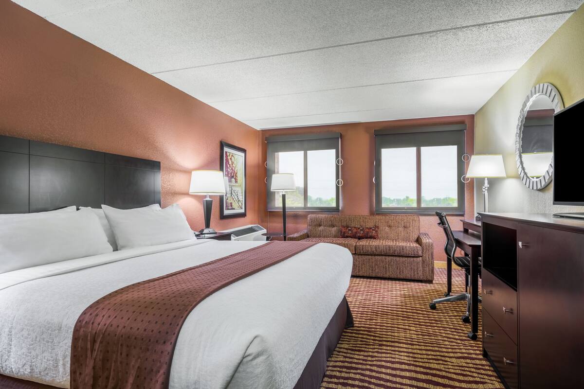 A hotel room with a large bed, a sofa, a desk, and a television.