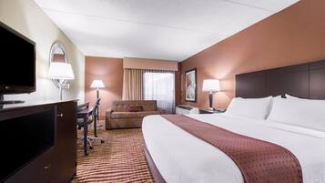 A hotel room with a bed, a desk, a chair, a TV, and a lamp.