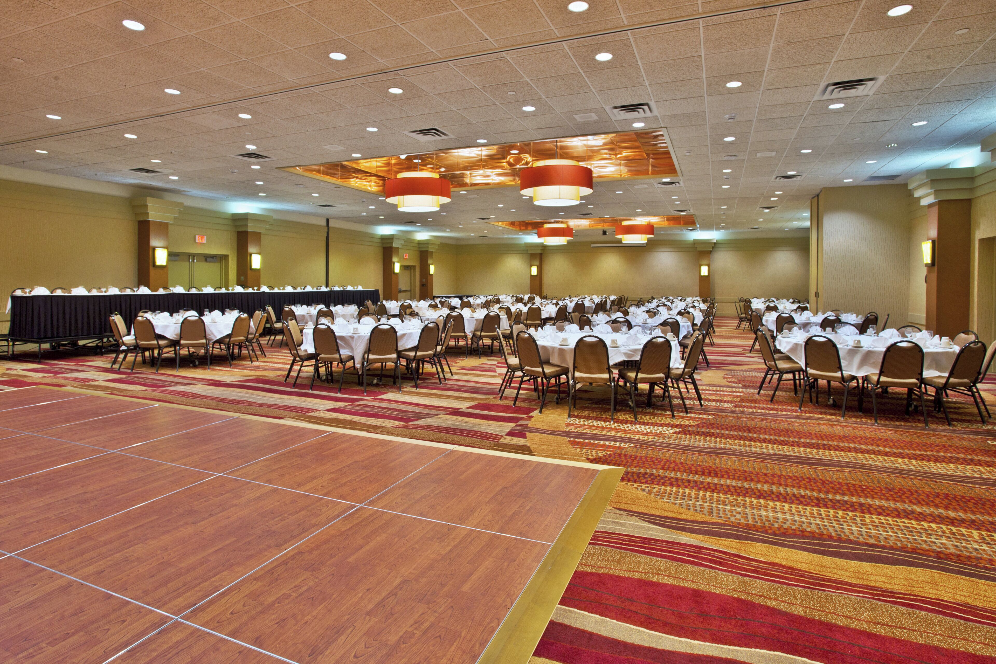 A large conference room with multiple round tables, chairs, and a carpeted floor.