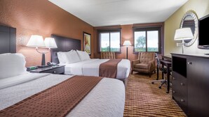 A hotel room with two beds, a desk, a chair, a TV, and a window.