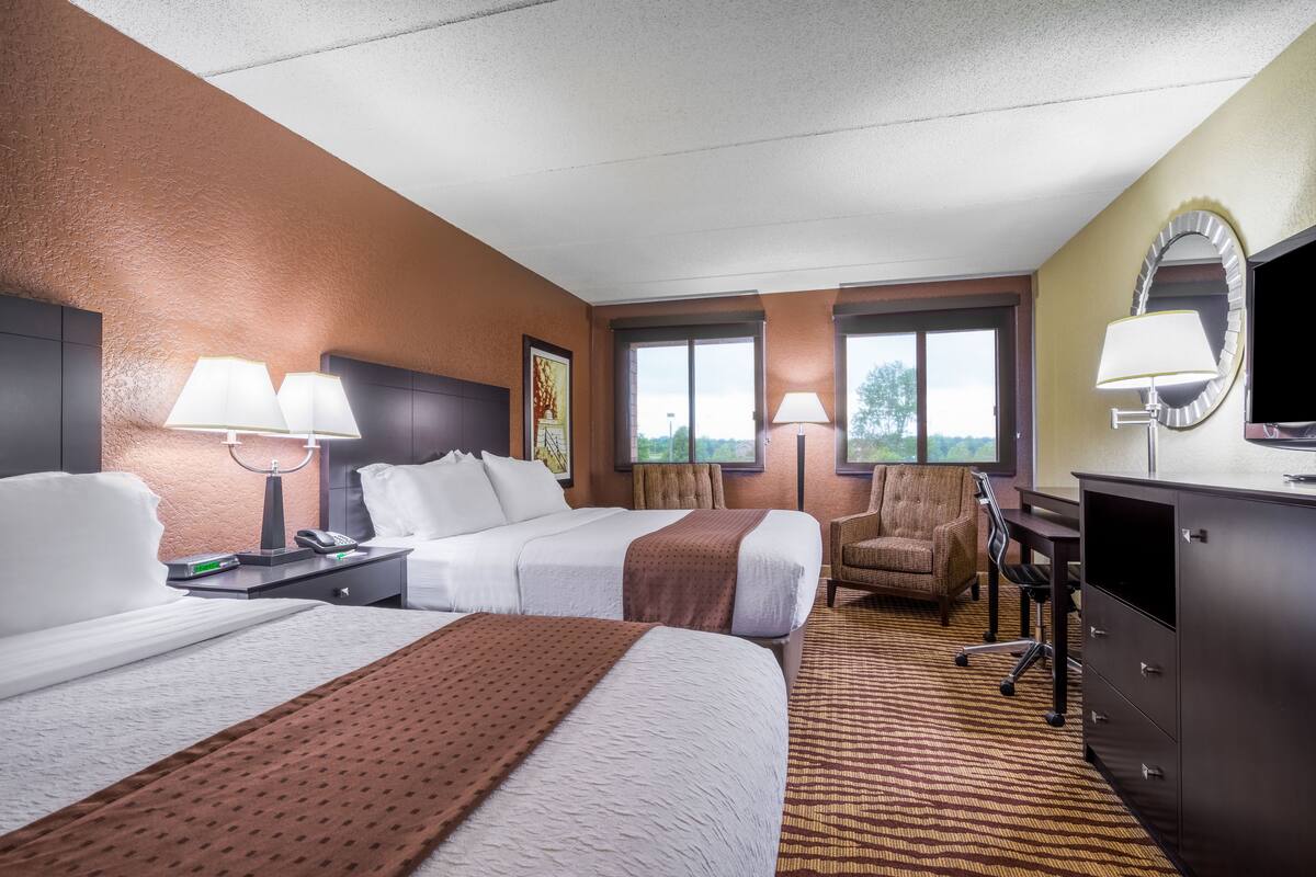 A hotel room with two beds, a desk, a chair, a TV, and a window.