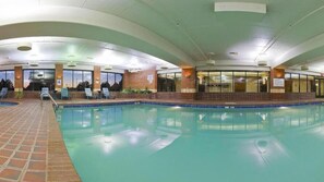 An indoor swimming pool with tiled flooring, lounge chairs, and a brick wall.