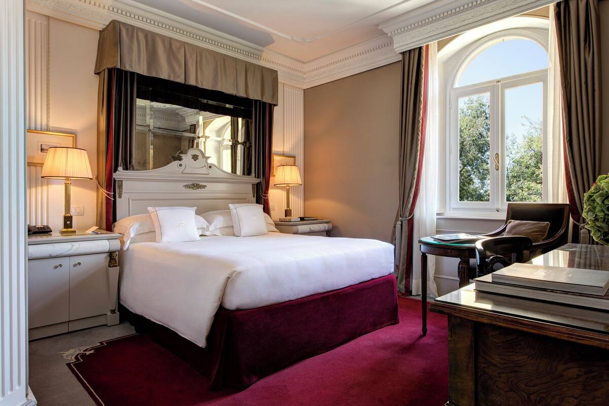 A well-appointed hotel room with a large bed, a desk, and a window with curtains.