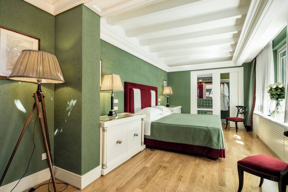 A hotel room with a bed, bedside tables, a lamp, a chair, and a window with a plant.