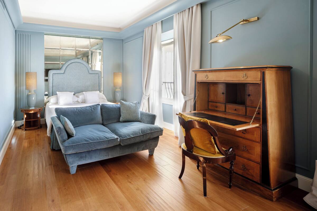 A bedroom with a bed, a sofa, a wooden dresser, and a desk.