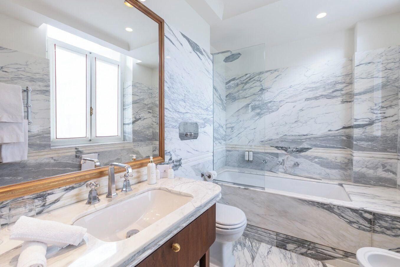 Un bagno con un mobile lavabo in marmo, uno specchio grande, una vasca da bagno e uno spazio doccia.