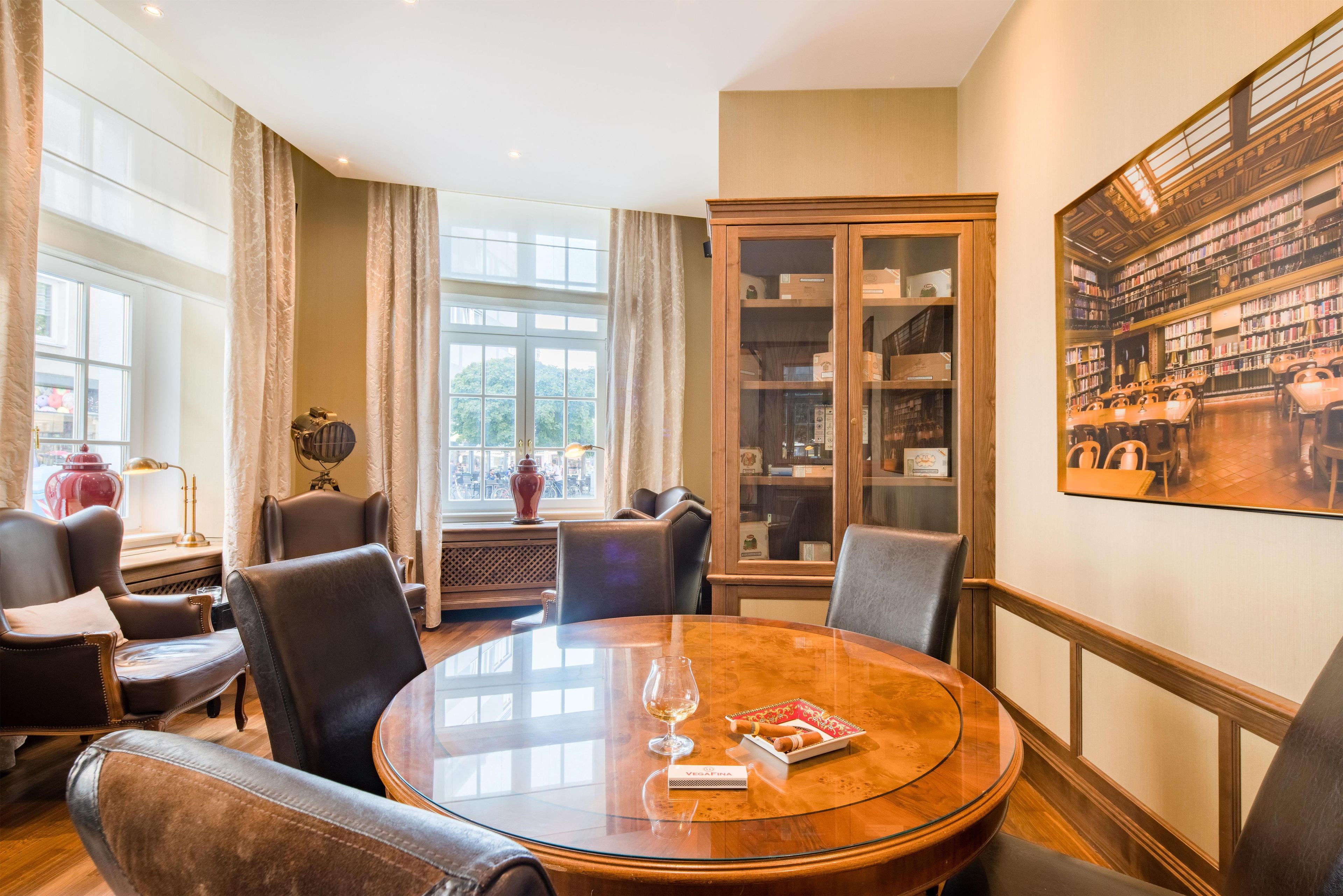 A conference room with a round table, leather chairs, a bookshelf, and a large window with curtains.